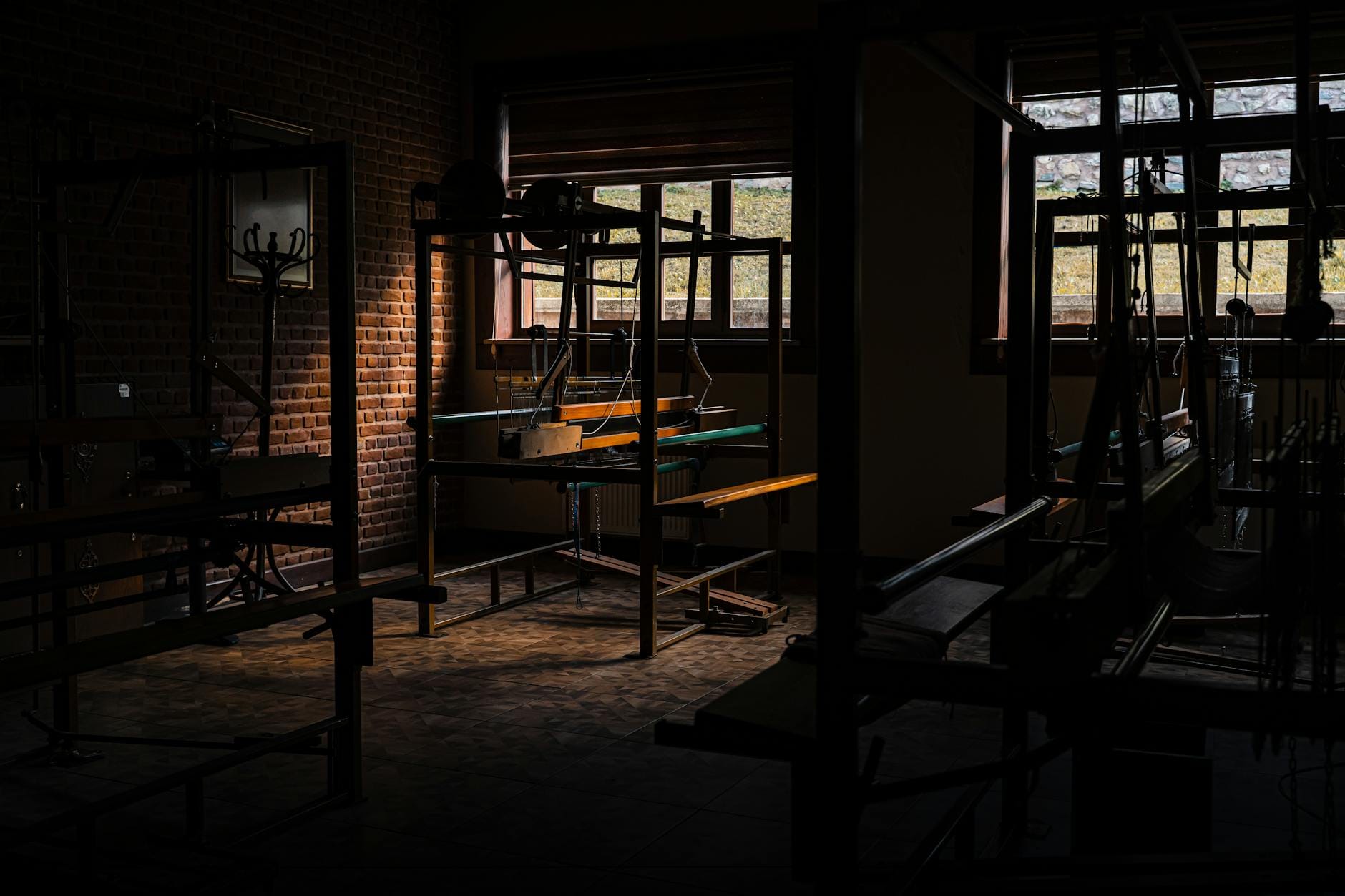 Ciemny warsztat tkacki z pustymi krosnami i ceglaną ścianą