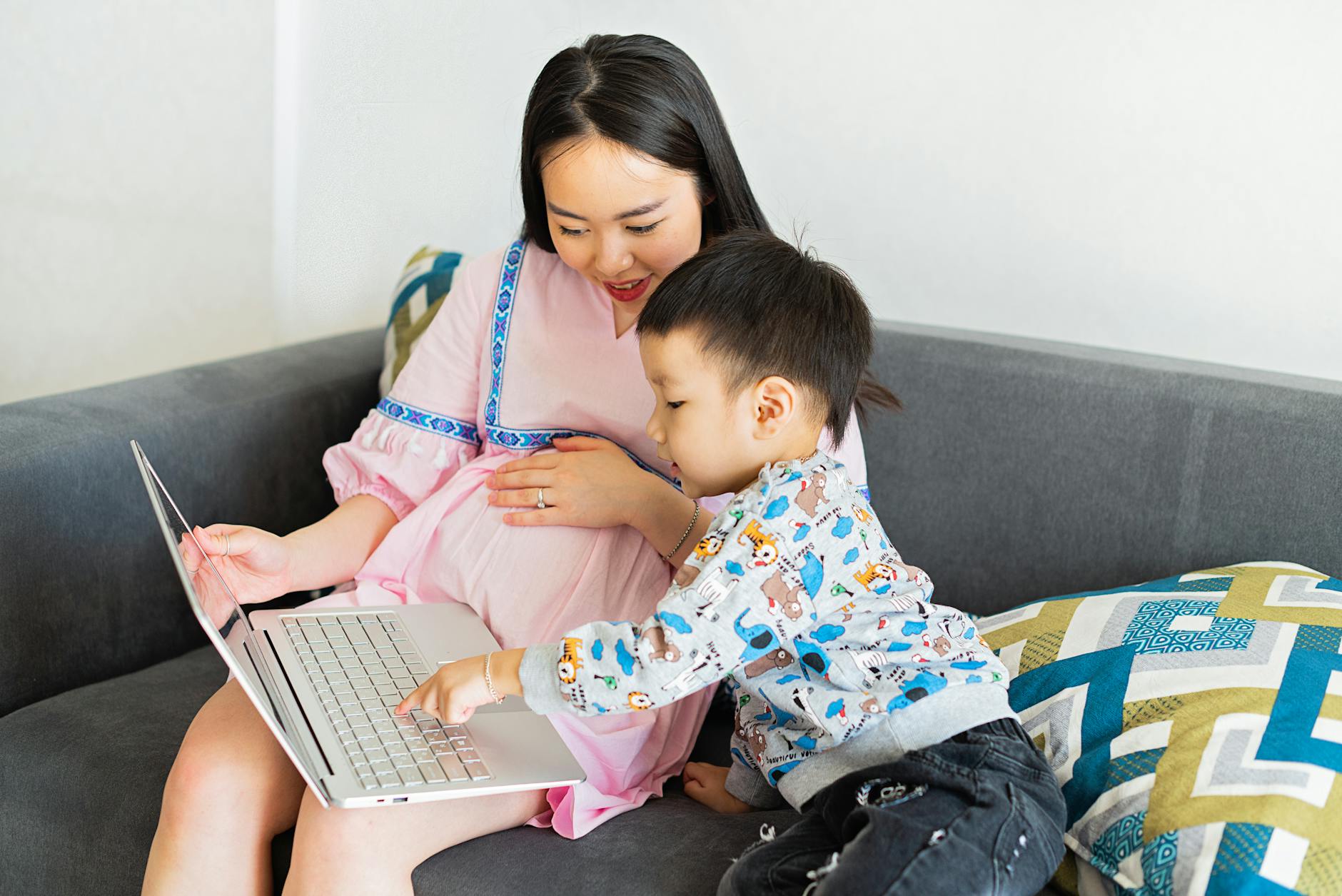Ciężarna mama z małym synem na kanapie oglądają coś na laptopie