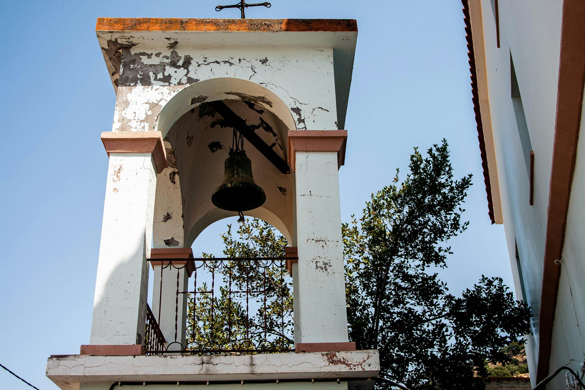 Stara drewniana dzwonnica z łuszczącą się farbą wśród zieleni