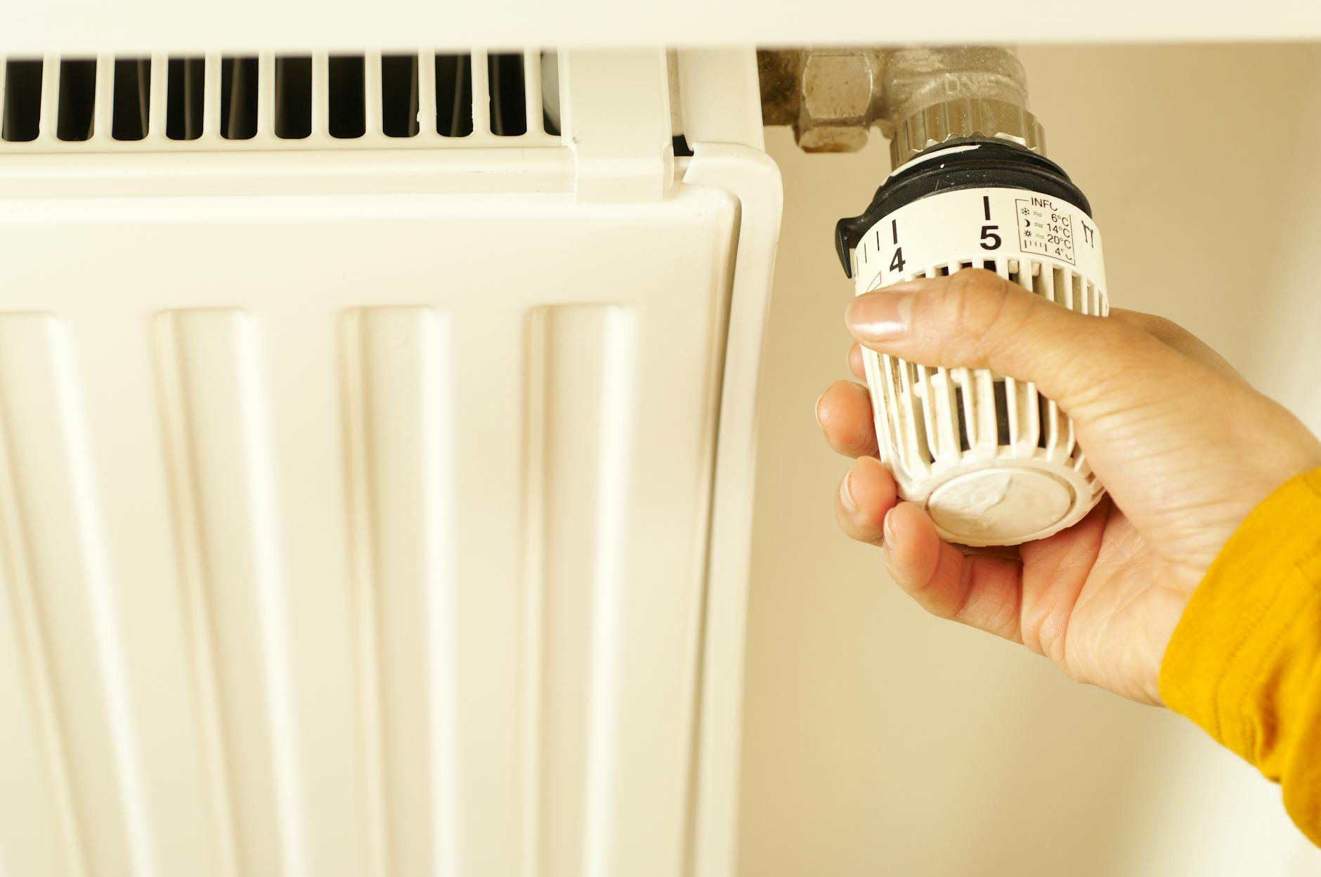 Dłoń regulująca termostat grzejnika w domowej instalacji ogrzewania