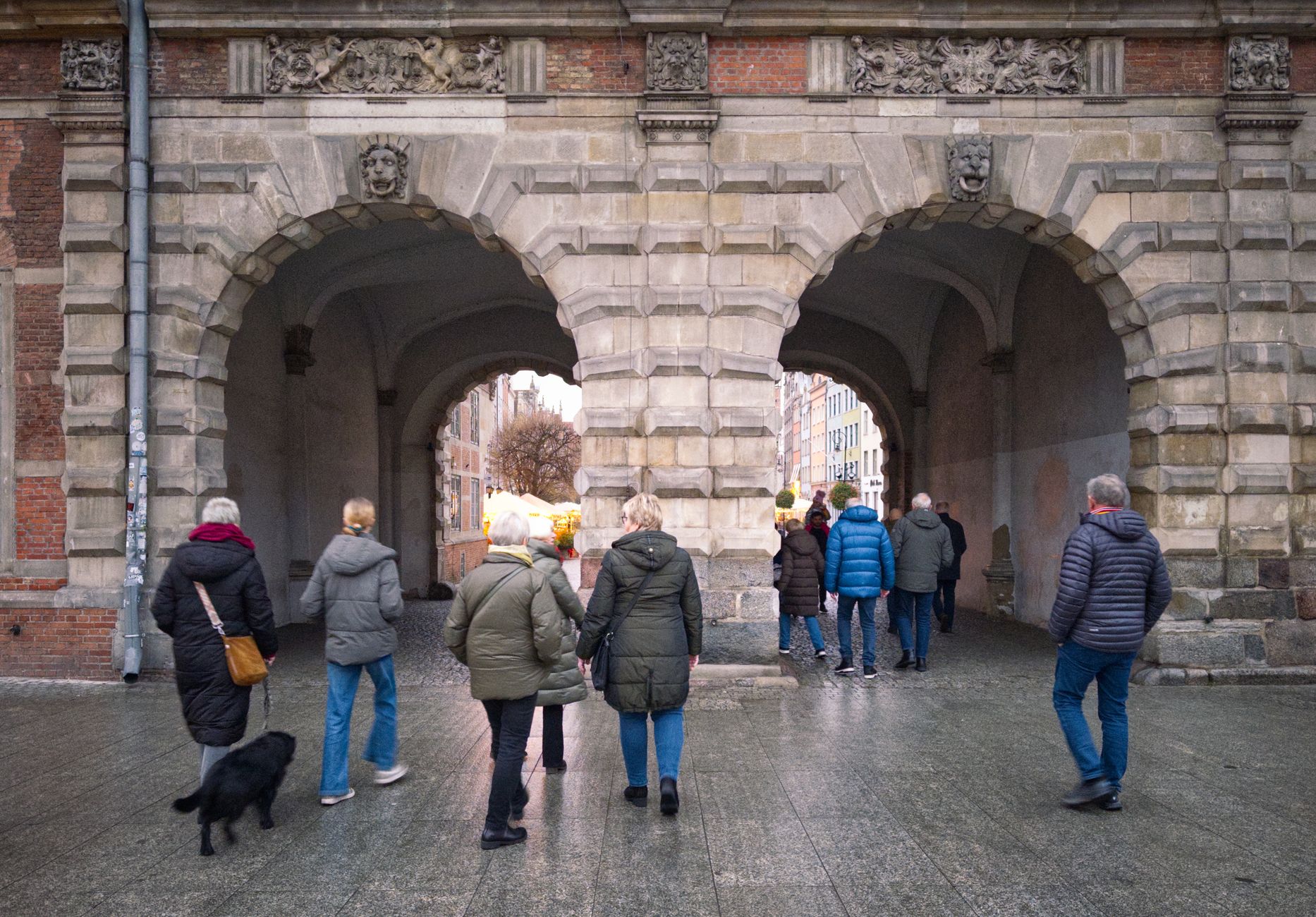 Turyści przechodzą przez zabytkową kamienną bramę miejską